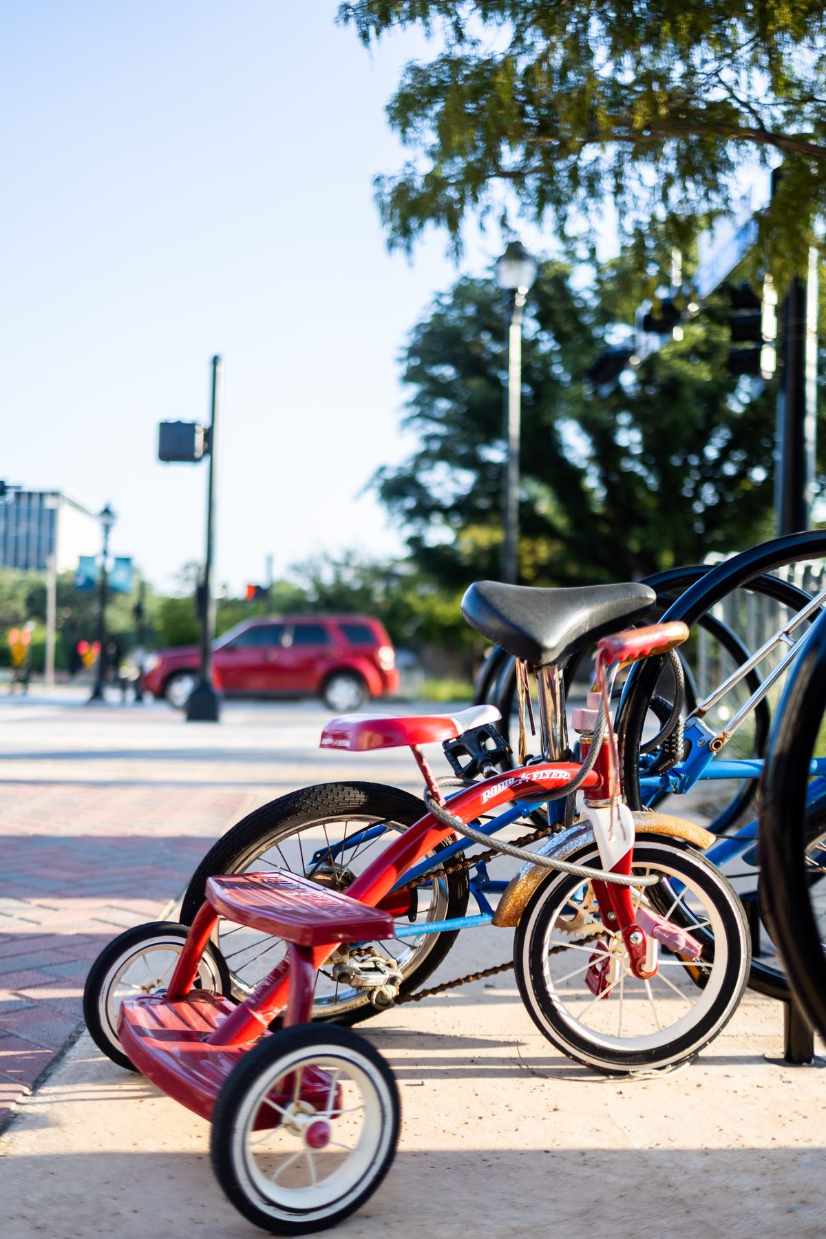 A child's red tricycle and bicycle parked at a bike rack on a sunny day